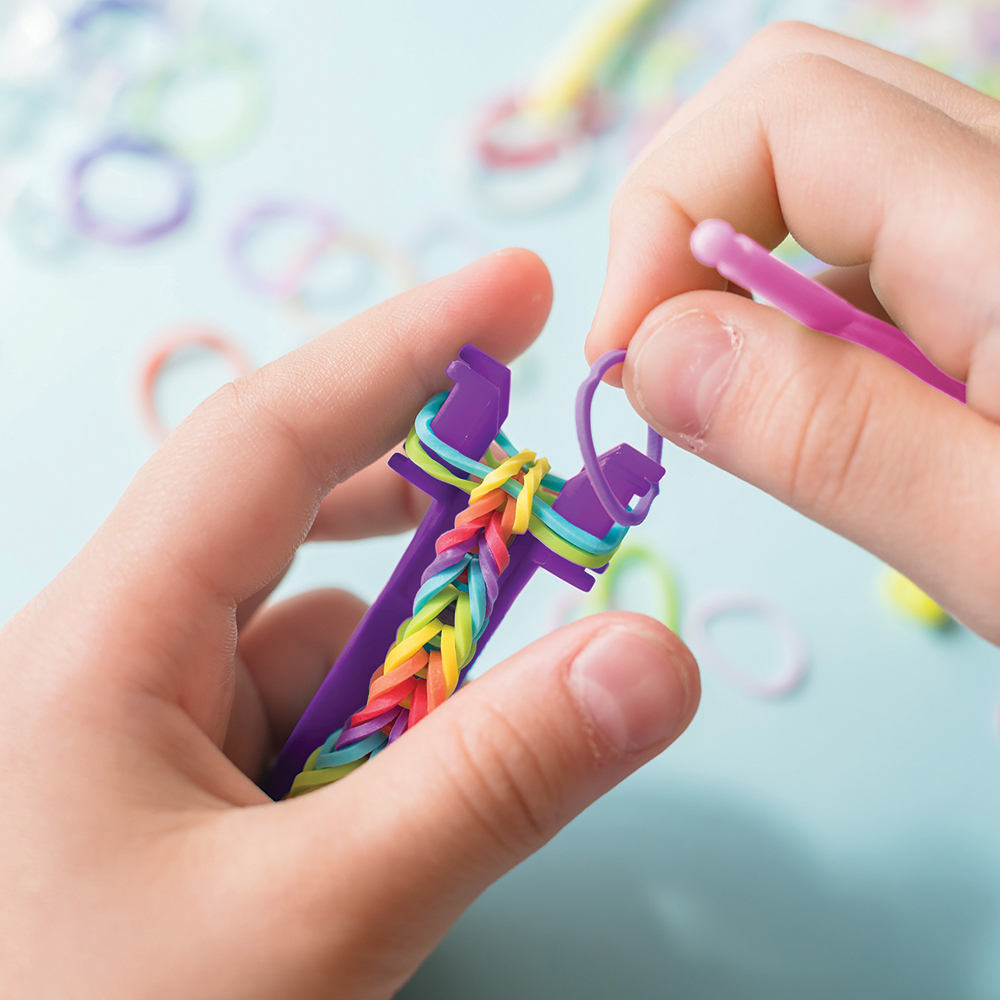 A girl makes a rainbow bracelet from rubber bands crochet. Closeup of making decorative bracelet with elastic bands. Loom bracelets