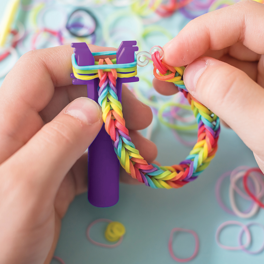 A girl makes a rainbow bracelet from rubber bands crochet. Closeup of making decorative bracelet with elastic bands. Loom bracelets
